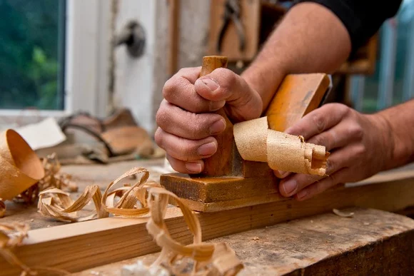Person hobelt Holz mit Hobel